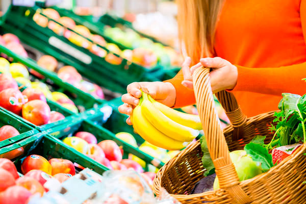 Девушка кладет бананы в корзину в супермаркете 