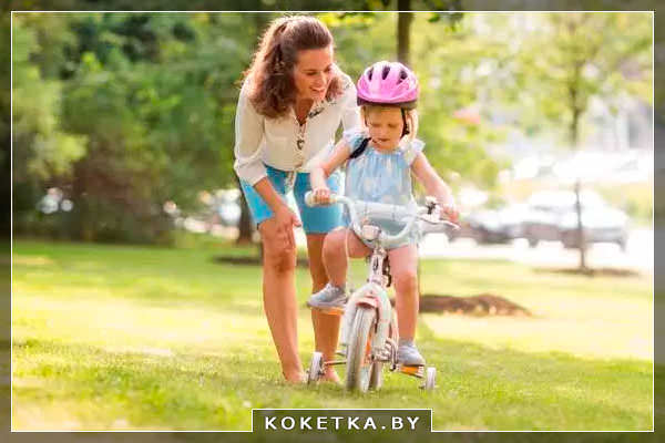 Мама учит ребенка ездить на велосипеде с боковыми колесами 